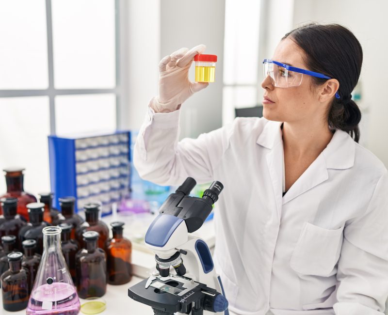 Young beautiful hispanic woman scientist holding urine test tube at laboratory